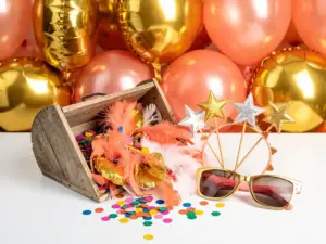 Colorful birthday photo booth corner with feather boas, oversized sunglasses, star wands, and gold foil balloons above a confetti-filled prop box.