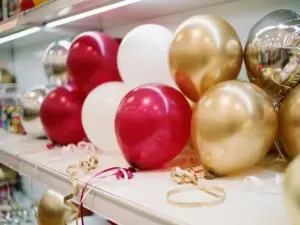 Kleurrijke, matte latex- en metallic Folieballonnen rood, wit en goud, uitgestald op een schap in een feestwinkel, met daaronder krullend lint.